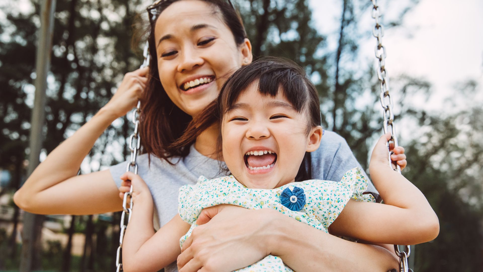 Mom & toddler swinging on swing joyfully in park