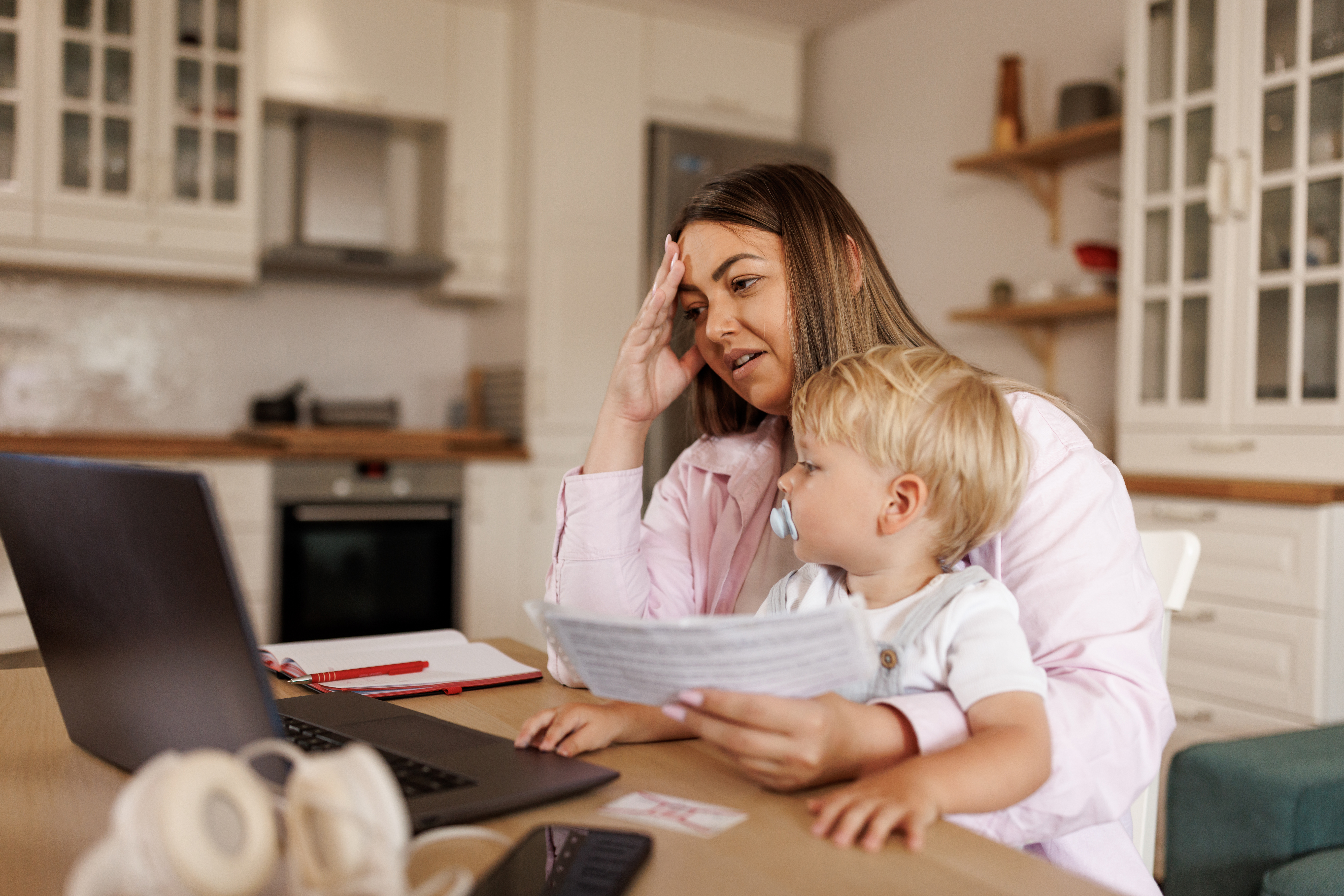 Worried single mother holding baby boy in her lap while looking at her computer screen.