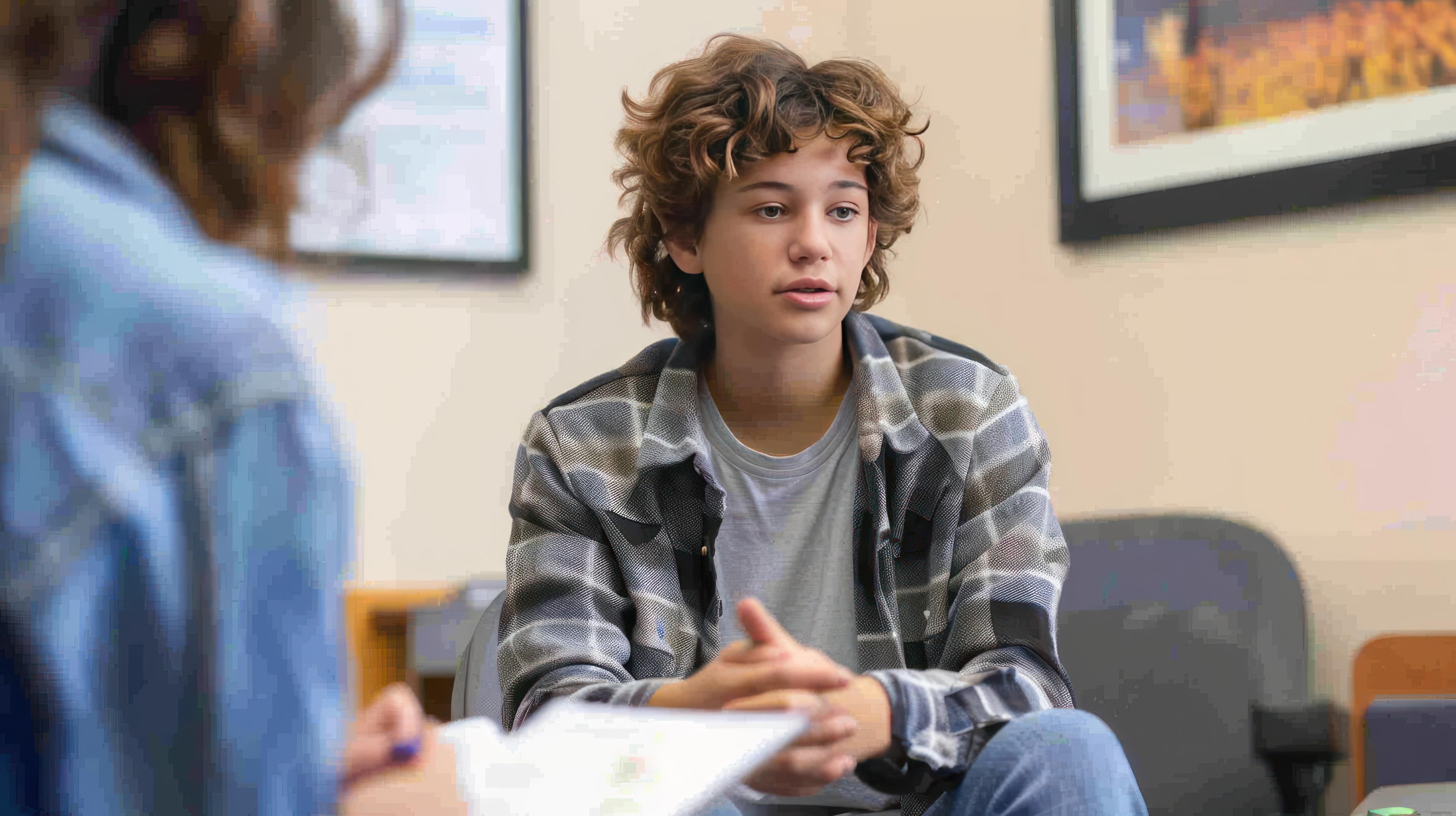 A curly-haired teenager talking to a professional, representing an individual seeking NDIS support for ADHD