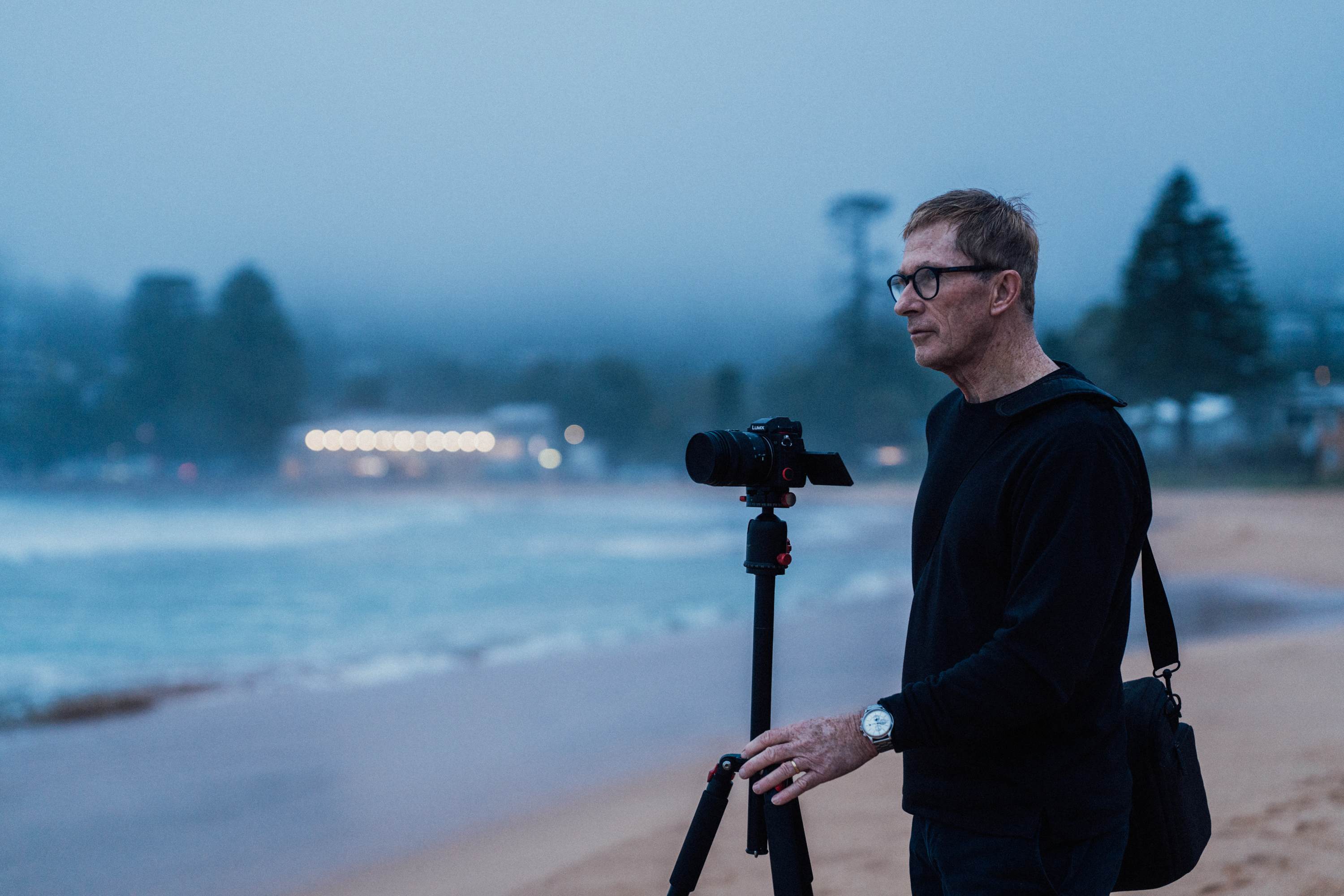 NDIS participant Richard using a professional camera to take photos on the beach on a gloomy, moody day.