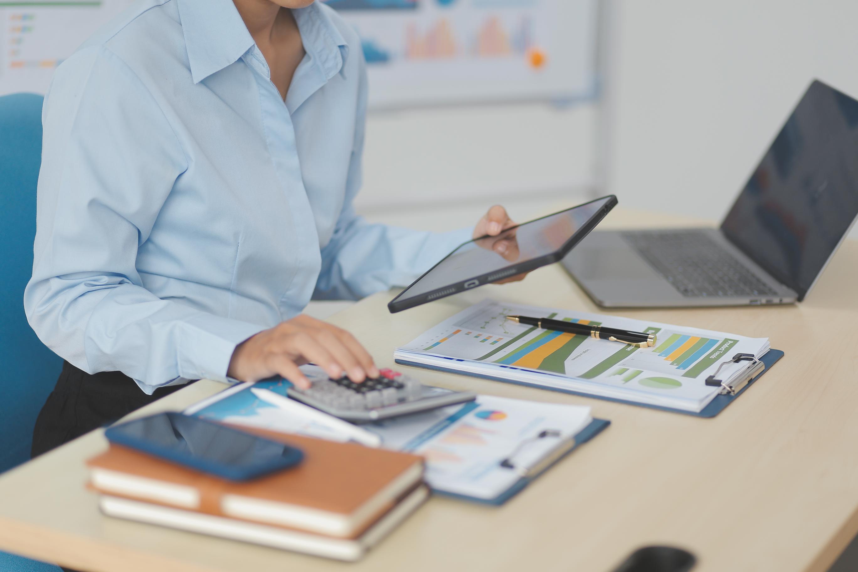A person uses a calculator, tablet, and printed charts to track an NDIS budget and manage funding.